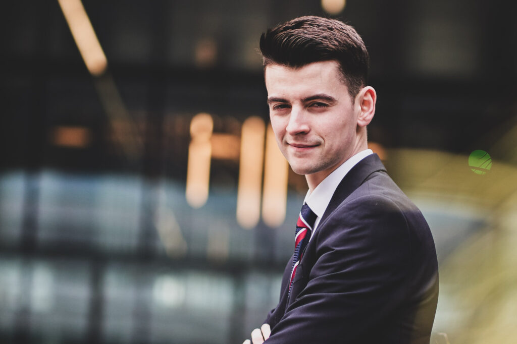 Business portraits of a young business person standing outside with arms folded against a glass fronted office