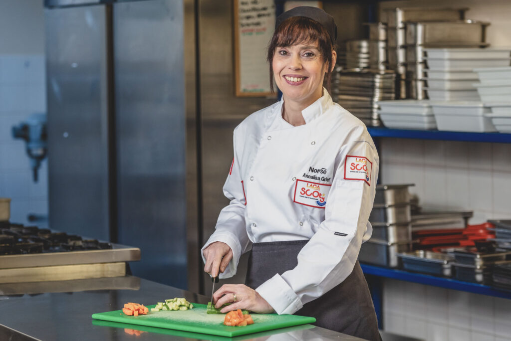 Relaxed Commercial Headshot Photography of a Norse Group Chef, wearing chefs whites and standing in a school kitchen preparing vegetable - Photography Norwich by Blanc Creative