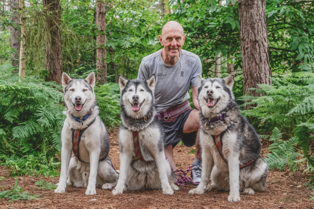 Runner Neil Feathery posing with a pack of husky dogs in a Norfolk forest, A natural environmental portrait - Blanc Creative