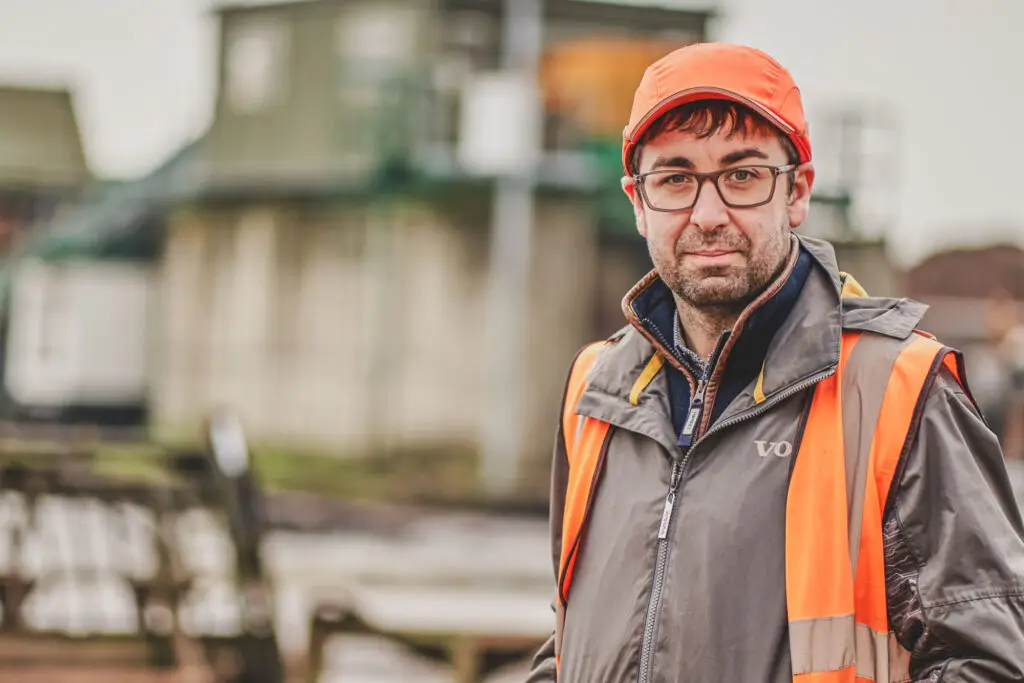 Male worker, orange hi-vis, moody natural light, industrial background — environmental portrait photography for trades and industry by Blanc Creative