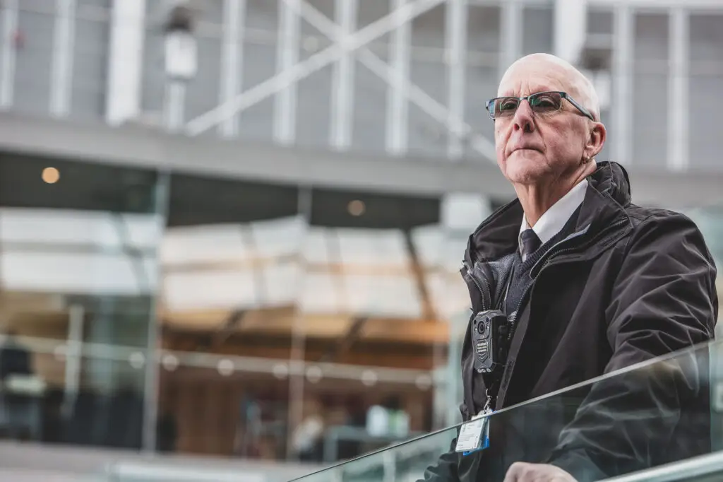 Male security officer environmental portrait, modern atrium interior, body camera, shallow depth of field — Norse Group corporate portrait photography Norwich by Blanc Creative