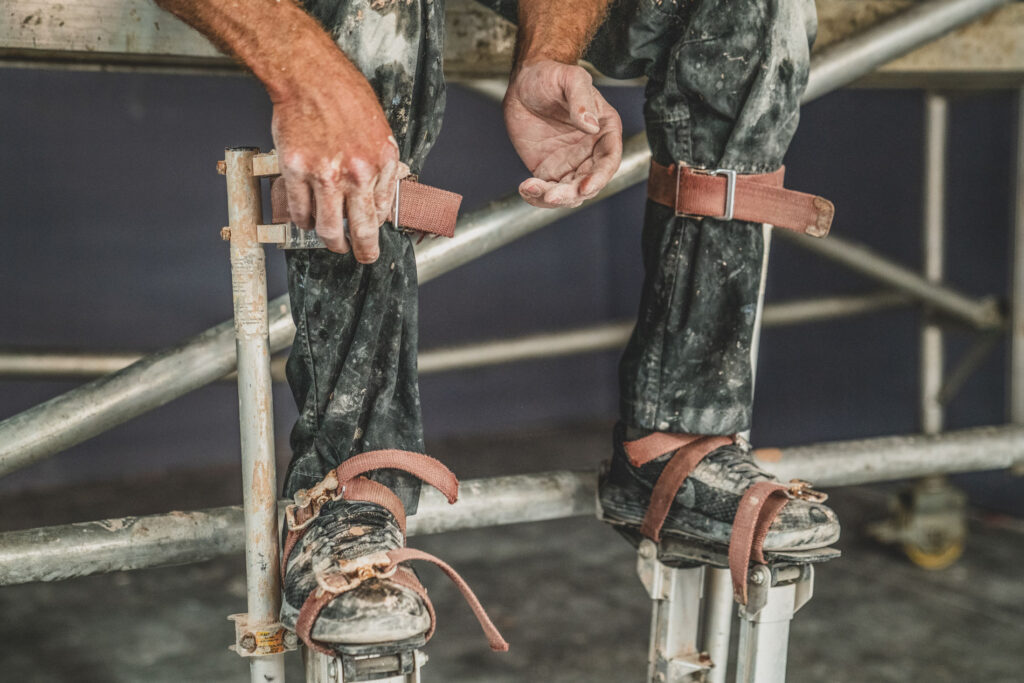 A plasterer puts on stilts to work on a high ceiling on a construction site. Construction Industry Photography Norwich