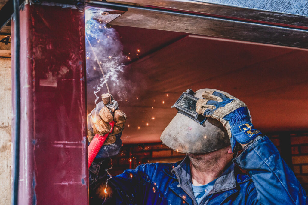 A welder wearing a mask works on metalwork on a building site - Norwich Construction Industry Photography from Blanc. Creative Norwich