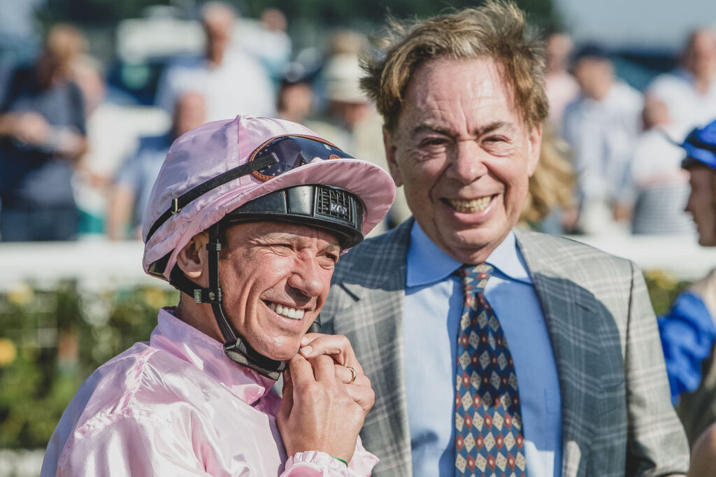 An editorial image of rocket Frankie Dettori with Sir Andrew Lloyd Webber at a horse racing meeting. Frankie Dettori is about to race and is fastening his chin strap and Andrew Lloyd Webber is laughing - Lee Blanchflower Norwich Photographer for Blanc Creative 