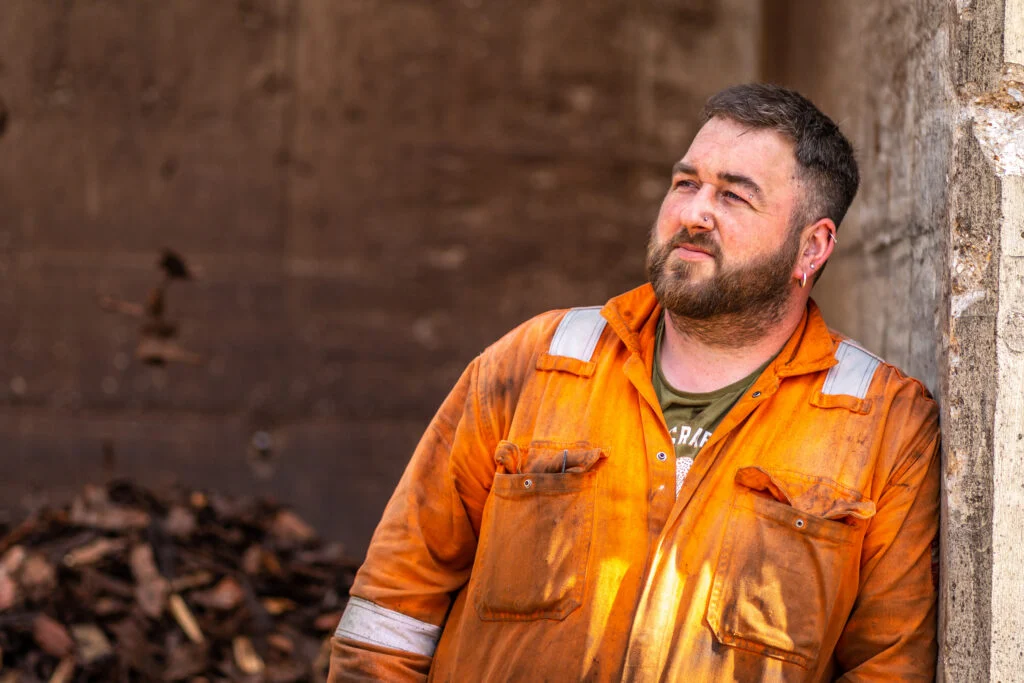 Male worker, orange hi-vis, moody natural light, industrial background — environmental portrait photography for trades and industry by Blanc Creative