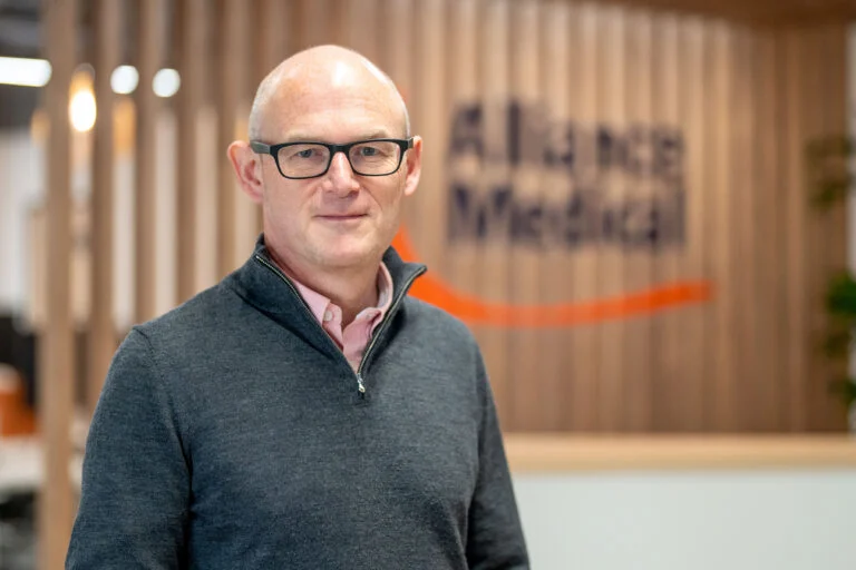 Male executive portrait, glasses, Alliance Medical branded backdrop, Warwick — environmental business portrait photography by Blanc Creative