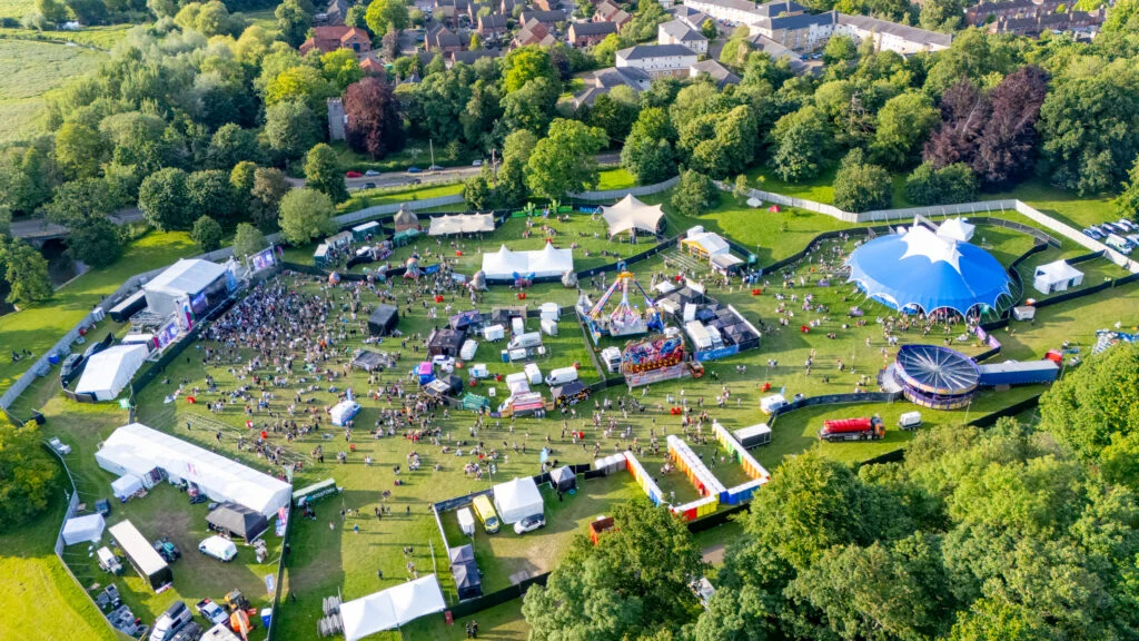 Aerial drone shot of an event site flown from open ground rather than over the crowd. Flying a Drone Over a Crowd: Why You Don't and What It Costs If You Do
