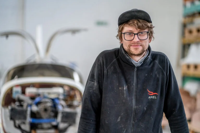 A young male aircraft engineer standing in the workshop with an aircraft behind him - Recruitment Photography