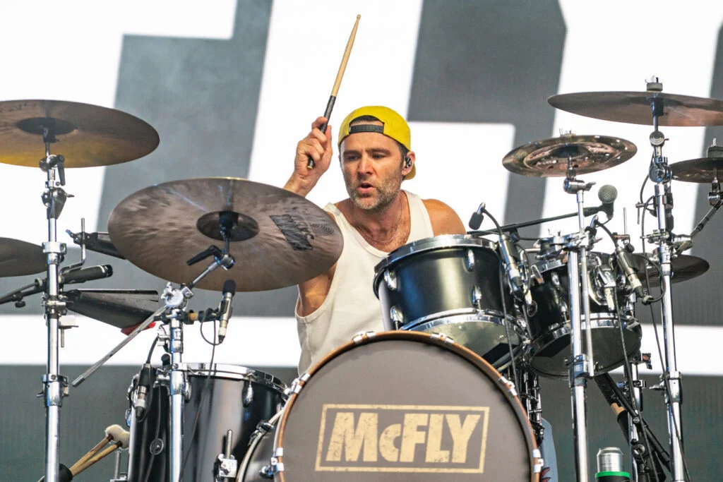 Harry Judd on drums in front of the McFly backdrop, Thetford Forest