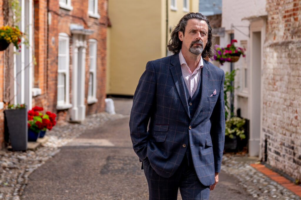 Business portrait Photography Norwich, Danny Kett in a navy suit walking a cobbled lane