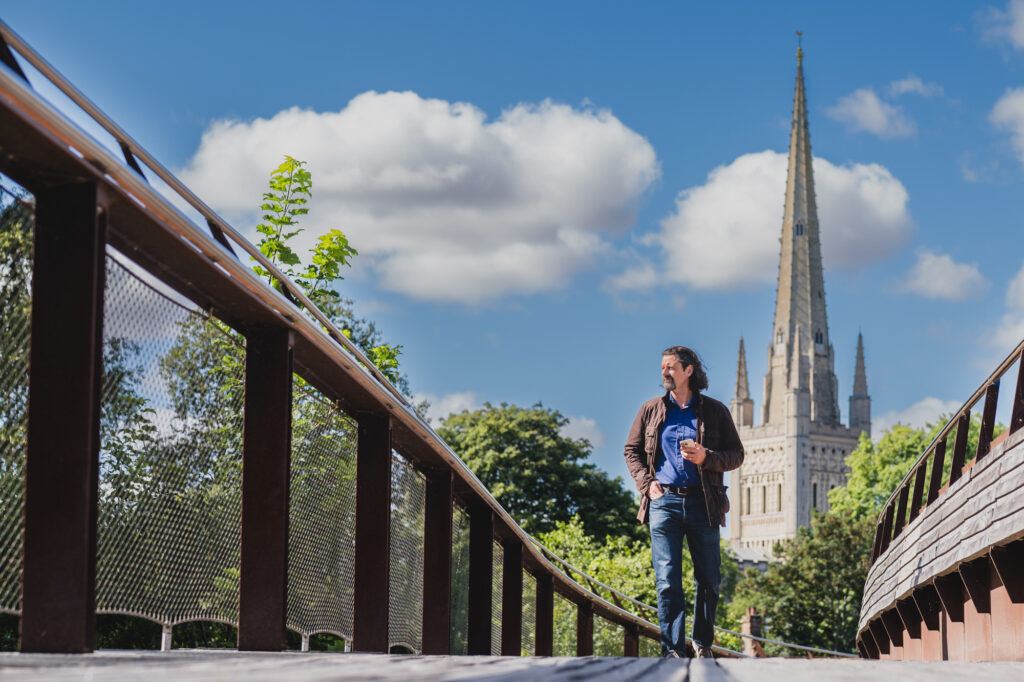Business portrait photography in Norwich, Dr Danny Kett on a footbridge with the cathedral spire behind